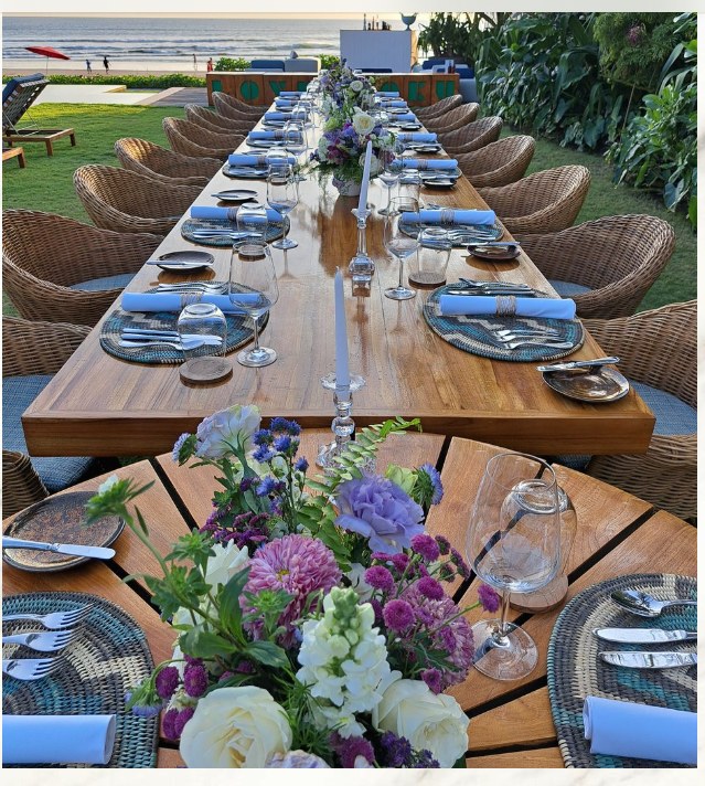 A long table set for a private dinner by the ocean at sunset